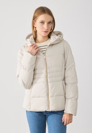 Polstret beige jakke med hette, gullglidelås og elastiske mansjetter. Har horisontal søm og en glattere, myk tekstur.