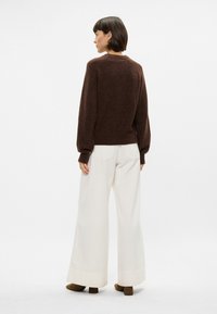 Καφέ πλεκτό πουλόβερ με χαλαρή γραμμή και ριμπ μανσέτες, συνδυασμένο με φαρδιά λευκά παντελόνια και καφέ σουέτ μποτάκια μέχρι τον αστράγαλο.