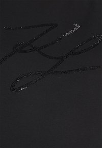 Tissu noir à surface texturée orné de paillettes noires scintillantes formant un motif cursif sur le matériau.
