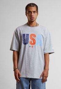 Gray oversized t-shirt made of cotton with a colorful "USA" graphic featuring blue, orange, and purple text, and star accents.