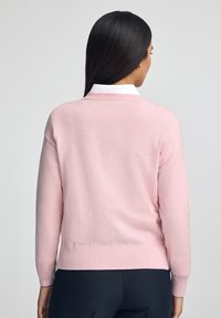 Maglione rosa chiaro realizzato in morbido tessuto a maglia, con scollatura rotonda, maniche lunghe e polsini e orlo a coste.