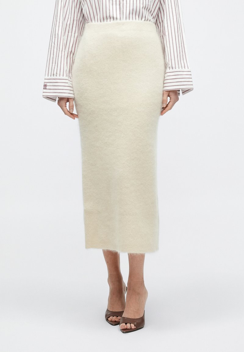 Woman wearing a cream fuzzy midi pencil skirt, striped long-sleeve shirt, and brown open-toe high heel shoes, standing against white background.