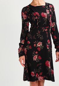Vestido negro con mangas largas, que presenta un estampado floral de rosas rojas y rosas, y una tela texturizada con un corte relajado.
