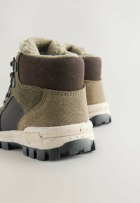 Bottes de randonnée marron et vertes avec une tige en daim et en maille texturée, doublure en polaire et semelle en caoutchouc robuste avec de profondes rainures.