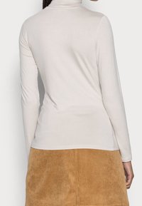 Vaaleanbeige pitkähihainen poolopaita pehmeästä kankaasta, istuva malli ja sileä pinta, yhdistetty ruskeaan corduroy-hameeseen.