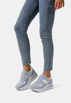Sneaker azzurro chiaro realizzati in materiali scamosciati e in rete, con dettagli grigi, una suola intermedia bianca spessa e un sistema di allacciatura, abbinati a jeans in denim.