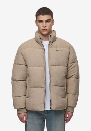 Beige puffjakke med quiltedesign, høy krage, glidelås foran og ribbestrikkede mansjetter. Har "PEGADOR"-logo i svart på venstre bryst.
