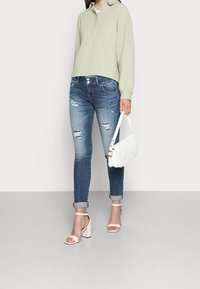 Sweatshirt texturé vert clair, jeans bleus déchirés, sac à main matelassé blanc et sandales à talons carrés beiges. Manches retroussées sur les jeans.