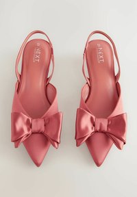 Chaussures à talons rose satinées avec un bout pointu et un grand nœud sur le devant. Texture lisse et design à talon ouvert.