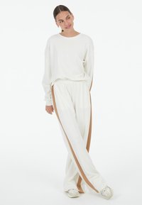 White sweatshirt with dropped shoulders and matching white pants featuring brown side stripes. Soft fabric with a relaxed fit and elastic waistband.