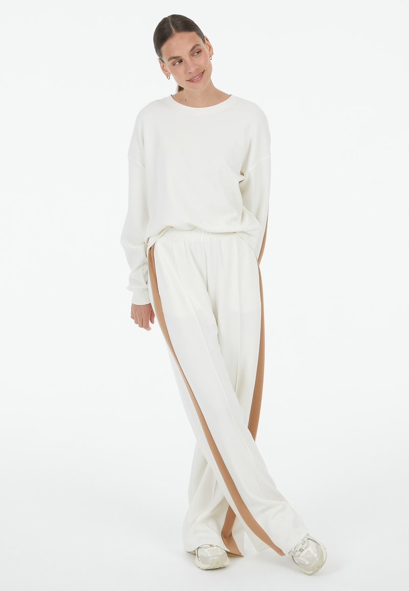 White sweatshirt with dropped shoulders and matching white pants featuring brown side stripes. Soft fabric with a relaxed fit and elastic waistband.