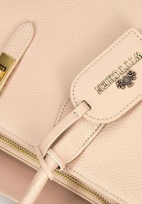 Bolso de mano de cuero rosa claro con textura de grano, herrajes dorados y una etiqueta con el logo. El cierre de cremallera cuenta con acentos dorados a lo largo del borde.