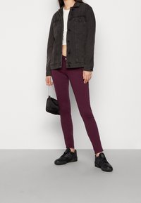 Svart denimjacka med framfickor, kort vit topp, vinröda slim fit-jeans och svarta sneakers. Liten svart handväska med kedjestropp.