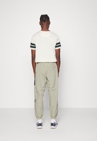 Krátký rukáv krémového trička s zelenými pruhy, spárovaný se světle zelenými kalhotami s elastickým pasem a bočním kapsou.