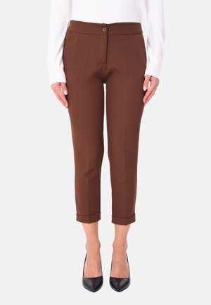 Pantaloni marroni su misura realizzati in tessuto liscio, con chiusura a bottone, lunghezza alla caviglia e orli arrotolati. Indossati con tacchi neri.
