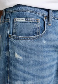 Heledad sinised teksad kulunud detailidega. Tagataskus on väike brändi silt ja kontrastne õmblemine. Standardne viie-tasku disain.