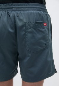 Shorts da bagno leggeri di colore blu navy realizzati in tessuto lucido. Presentano una vita elastica, una tasca sul retro e un piccolo etichetta rossa con il logo Diesel.