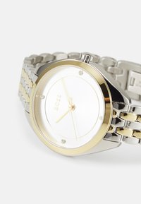 Montre en argent et or avec un cadran blanc minimaliste, trois accents en diamant et un bracelet en métal lié avec finition polie.