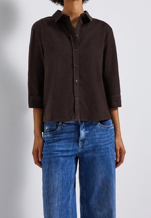 Bruine blouse met lange mouwen en knopen, met een kraag, gemaakt van textuurstof, gecombineerd met blauwe jeans met rechte pijpen.