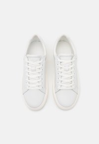 Baskets en cuir blanc avec lacets plats, bout arrondi, accents gris clair, et semelles texturées. Nom de la marque embossé sur les côtés.