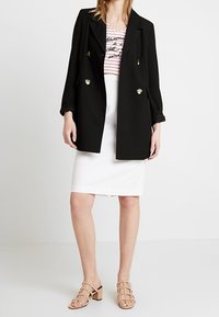 Sort dobbeltradet blazer med guldknapper, parret med en stribet t-shirt og hvid pencil skirt, afsluttet med beige sandaletter med stropper.