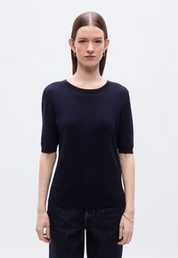 Μπλε σκούρο πουλόβερ με κοντά μανίκια και στρογγυλή λαιμόκοψη, με ριμπ λεπτομέρειες και λεία υφή, συνδυασμένο με σκούρο τζιν παντελόνι.