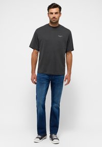 Camiseta de algodón gris oscuro con mangas cortas y cuello redondo, combinada con jeans de mezclilla azul y zapatillas negras con acentos blancos.