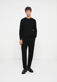 Schwarzer gerippter Pullover mit Rundhalsausschnitt, kombiniert mit schwarzen Hosen und schwarzen Slippern. Schlichtes, monochromes Ensemble mit lässiger Passform.