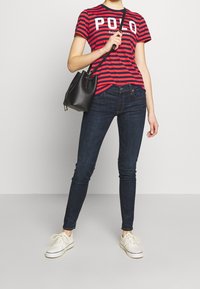 Röd och marinblå randig t-shirt med "POLO"-logotyp, mörkblå skinny jeans, vita sneakers och en svart bucket bag.