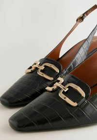 Musta nahkainen slingback-kengät, joissa on krokotiilimuotoinen pinta, kultasävyiset solkivarusteet ja teräväkärkinen muotoilu.