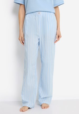 Woman wearing light blue and white vertical striped loose pants and a matching light blue top, standing barefoot against a white background.