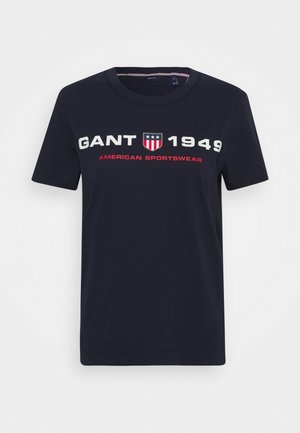 T-shirt in cotone blu navy con maniche corte, con testo audace bianco e rosso: "GANT 1949 AMERICAN SPORTSWEAR" e un logo a scudo.