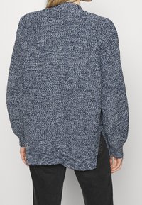 Texturerad marinblå stickad tröja med långa ärmar, sidofickor och en avslappnad passform. Tyget har ett melerat mönster.