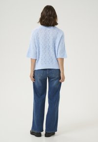 Gaiši zils adīts džemperis ar īsām piedurknēm, kuram ir reljefs chevron raksts, apvienots ar brīva griezuma tumši ziliem džinsiem un melniem platformu apaviem.