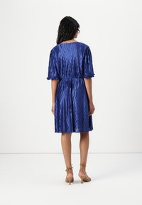 A knee-length, pleated blue dress with short puff sleeves and an elastic waist. Smooth texture with a subtle sheen, accessorized with tan heeled sandals.