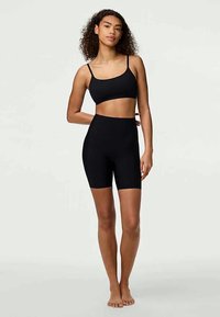 Conjunto de ropa deportiva negra que incluye un top corto con tirantes finos y pantalones cortos tipo biker de cintura alta, ambos confeccionados en un material suave y elástico.