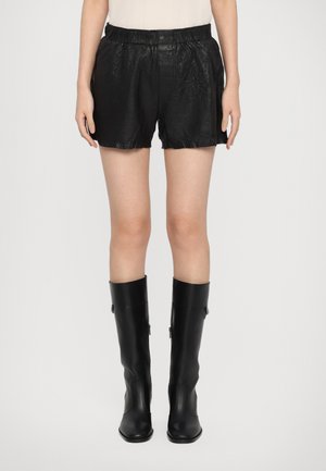 Svarta lädershorts med elastisk midja, med en skrynklig textur och en lös passform. Kombinationen är med höga svarta blanka stövlar.