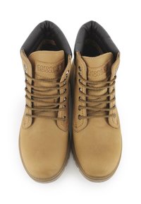 Botas de cuero marrón hasta el tobillo con forro negro, puntera redonda y ojales metálicos. Presentan costuras prominentes y un diseño tradicional con cordones.