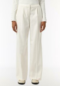 White, pleated trousers with a relaxed fit, featuring a smooth texture and subtle stitching details, paired with light-colored shoes.