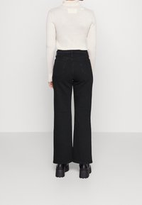 Svarta vida jeans med hög midja och två bakfickor, ihop med en krämfärgad ribbad polotröja. Stiliga klumpiga svarta platåstövlar.