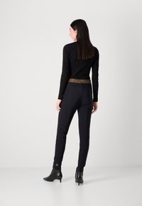 Top noir à manches longues avec un design ajusté, associé à un pantalon noir avec une ceinture imprimée léopard et des bottines noires.