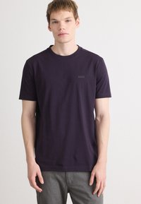 Μωβ μπλουζάκι με στρογγυλή λαιμόκοψη, φτιαγμένο από βαμβάκι, με μια διακριτική λογότυπο στο αριστερό στήθος και κοντά μανίκια. Λείος υφή, χαλαρή εφαρμογή.