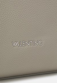 Šedá texturovaná kůže s embosovaným logem "VALENTINO" ve stříbrné barvě. Má hladký povrch a jemný vzor zrna.