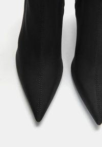Černé ankle boot s špičatou špičkou vyrobené z hladké kůže, s vertikálním švem a elegantním designem bez viditelného hardwaru nebo ozdob.