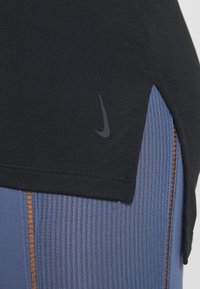 Top atletico nero con una fessura laterale e un piccolo logo Nike. Abbinato a leggings blu texture con righe verticali e accenti marroni.