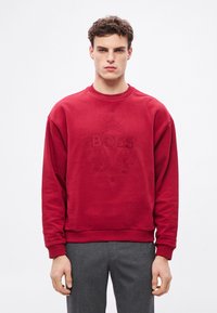 Κόκκινη φούτερ μπλούζα με στρογγυλή λαιμόκοψη, με ανάγλυφο σχέδιο λογότυπου "BOSS". Μακριά μανίκια και ριμπ μανσέτες, κατασκευασμένη από μαλακό ύφασμα.