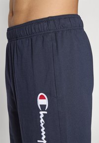 Marineblå treningsshorts i lett stoff. Har strikk i livet og brodert logo på siden i rødt, hvitt og blått.