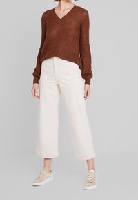 Sweater en tricot beige texturé avec un col en V, associé à un pantalon large off-white et des baskets beige clair.