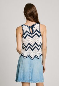 Bílý krajkový crop top s námořnickým zigzag vzorem, osmičkovým lemem a mašlí na zádech, v kombinaci s lehkou džískou sukní.