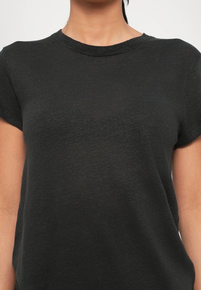 Mujer con una camiseta negra lisa de manga corta y cuello redondo, mostrada desde el cuello hasta la cintura sobre un fondo claro.